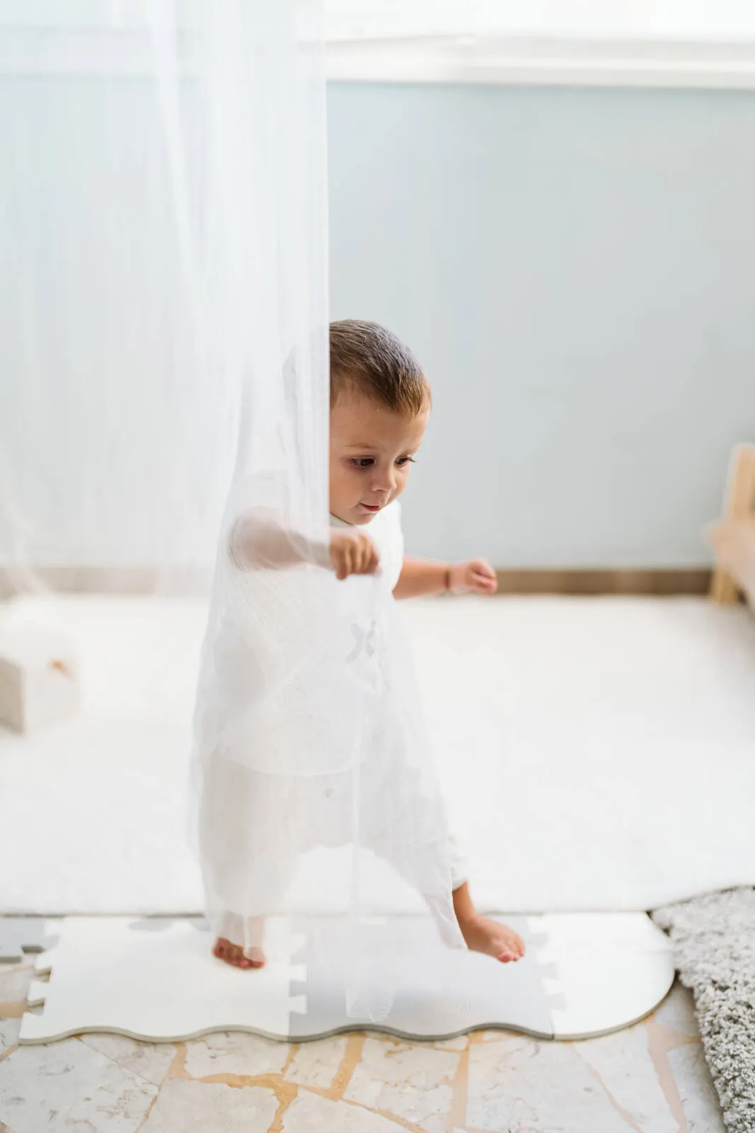 Bambino in piedi da solo dietro una tenda — inserimento al nido, il primo distacco