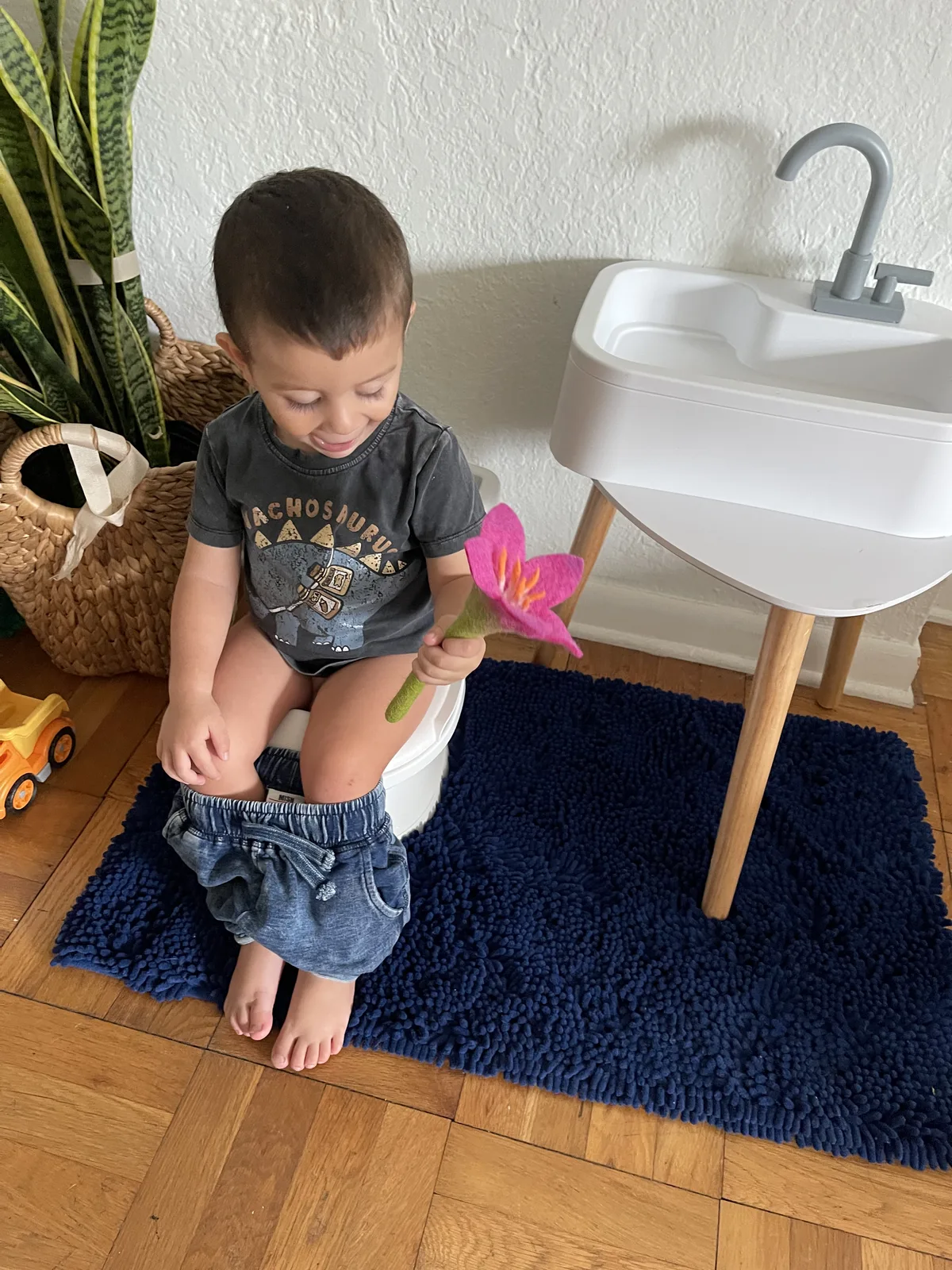 Bambino sereno seduto sul vasino con un fiore in mano durante lo spannolinamento